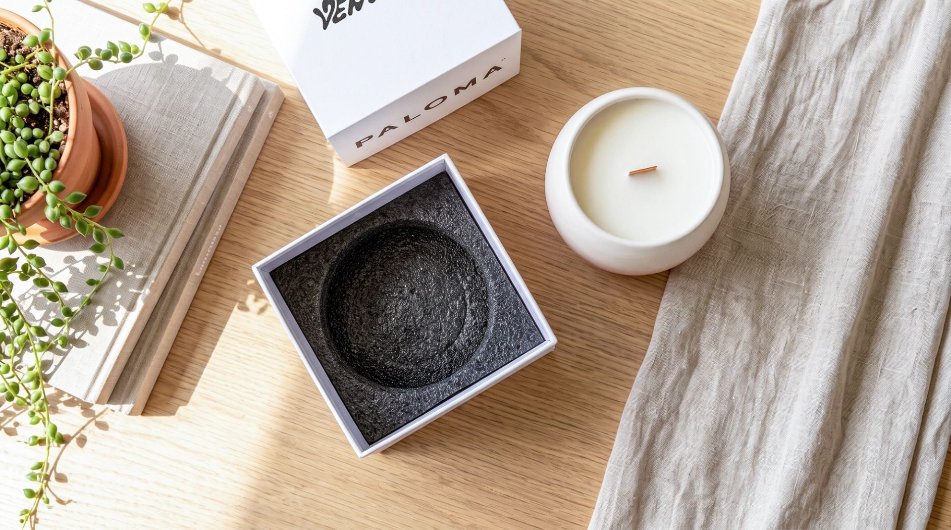 A top-down view of an unboxed white ceramic candle sitting next to its open white packaging box, which reveals a protective black EPE foam insert.