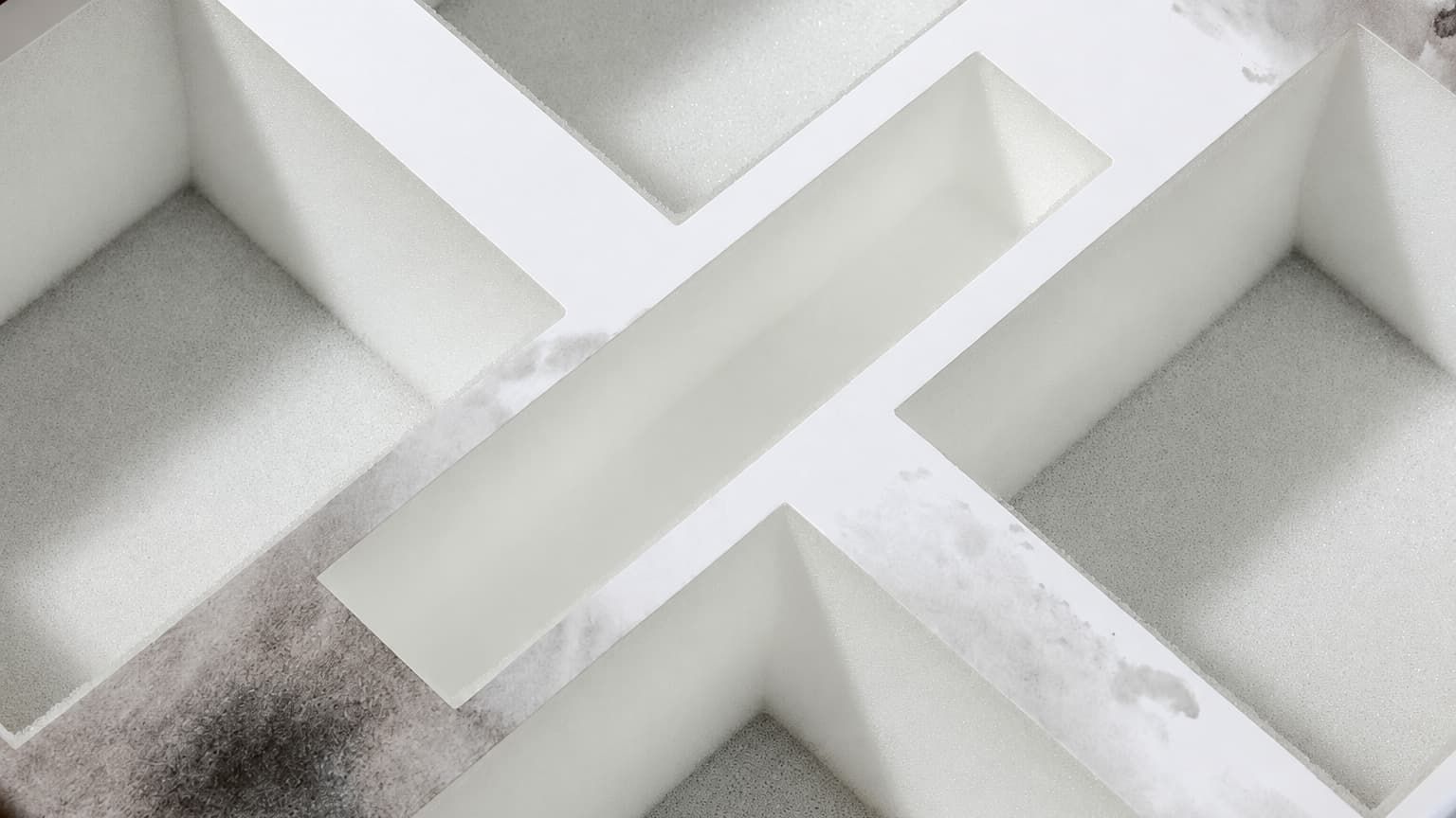 Close-up of an empty white foam insert inside a box with cross-shaped dividers to securely hold four candles.