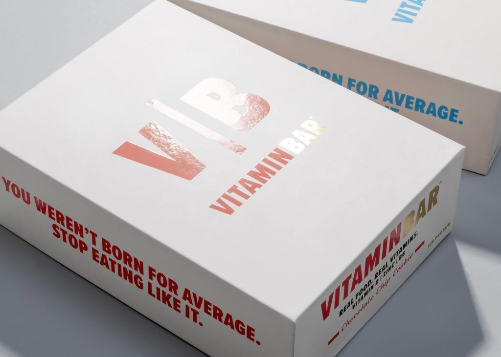Two stacked white Vitamin Bar boxes displaying foil logos and bold motivational text along the sides.