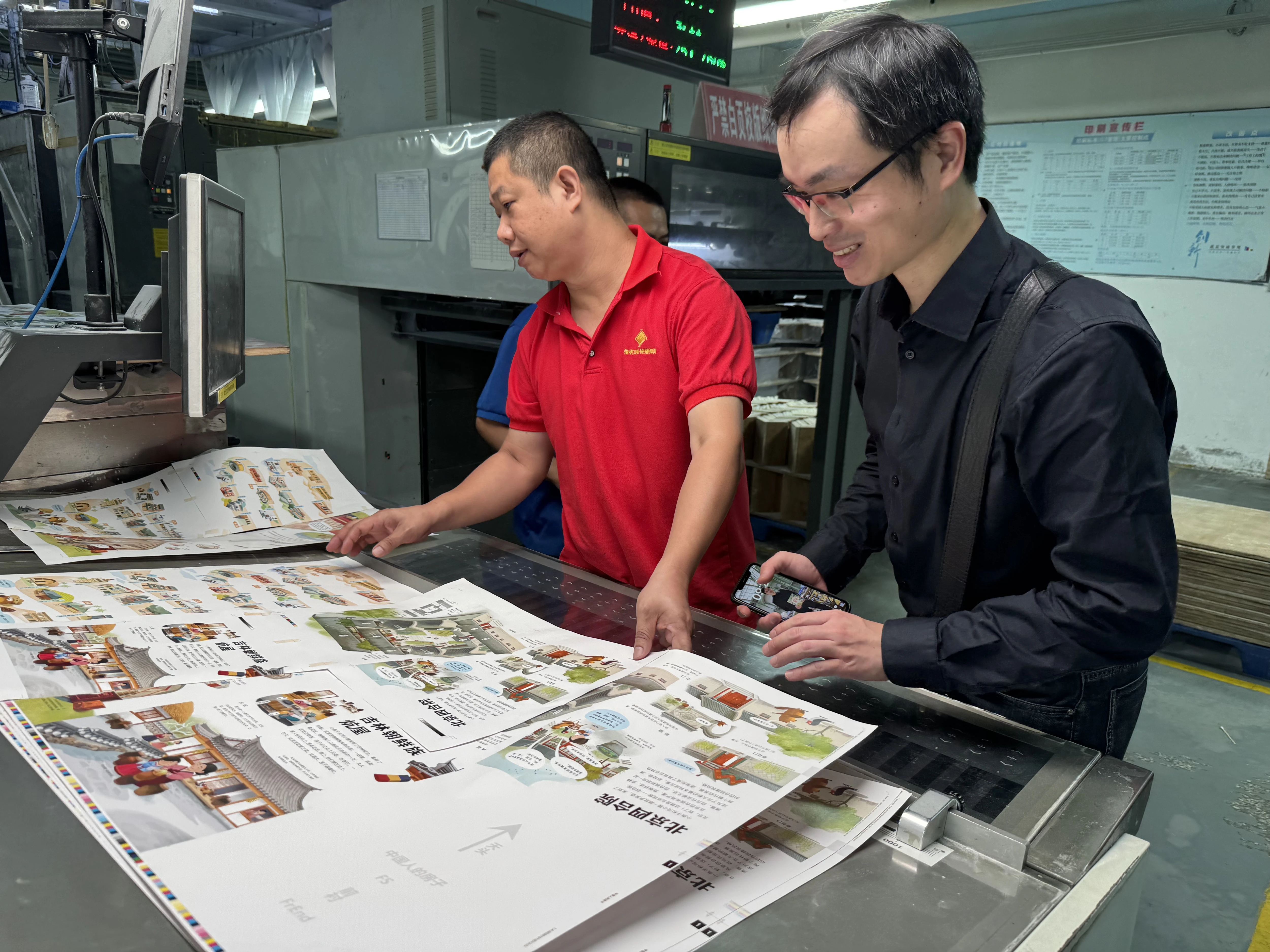 Two people checking a printed proof sheet at a printing press
